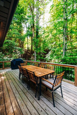 Una terraza de madera con una mesa y sillas, rodeada de un bosque.