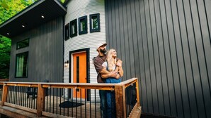 A modern house with a wooden deck, a circular section, and a bright orange door.