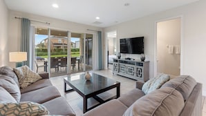 A modern living room with a sofa set, a coffee table, a TV, and a sliding glass door leading to an outdoor patio.
