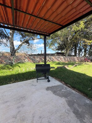 An outdoor patio area with a barbecue grill, a concrete floor, and a stone wall in the background.