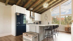 Una cocina moderna con armarios blancos, un refrigerador negro, un cofre de madera y una barra con taburetes.