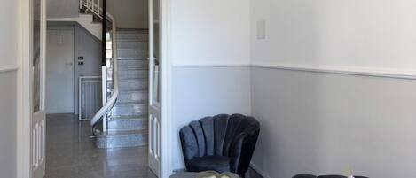 A hallway with a staircase, a small round table, two chairs, and a vase of flowers.