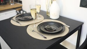 A dining table set with black plates, two glasses of white wine, and a vase with red roses. - La Romance Room - Jacuzzi | Cinema | Sauna (Arnouville)