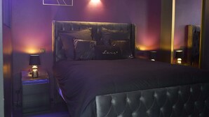 A modern bedroom with a tufted headboard, a large mirror, and ambient lighting. - La Romance Room - Jacuzzi | Cinema | Sauna (Arnouville)