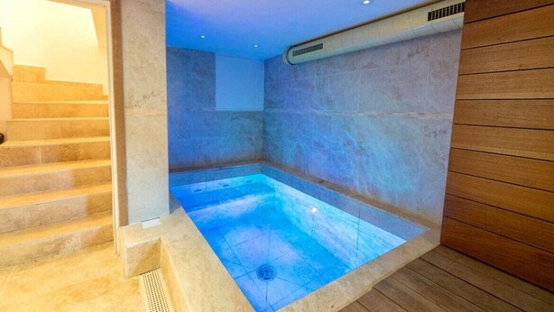 A spa room with a hot tub, wooden flooring, and a stone wall. - Cosy mountain house with heated pool (Beuil)