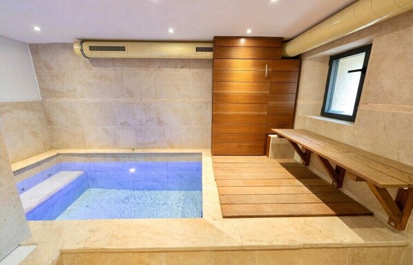 A modern spa room with a hot tub, wooden benches, and a small window.
