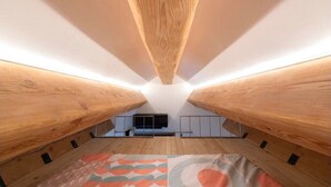 A room with a sloped ceiling and wooden beams, a television, and a patterned rug. - Cosy mountain house with heated pool (Beuil)