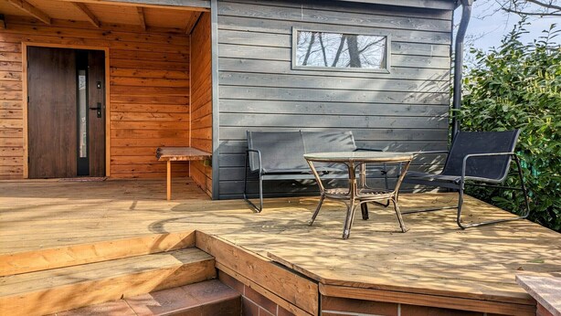 A wooden cabin with a patio area featuring a table and chairs, a bench, and a door leading inside. - Large holiday apartment with sauna (Kolobrzeg)