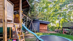 A wooden playhouse with a slide, a trampoline, and a small shed in a backyard. - Large holiday apartment with sauna (Kolobrzeg)