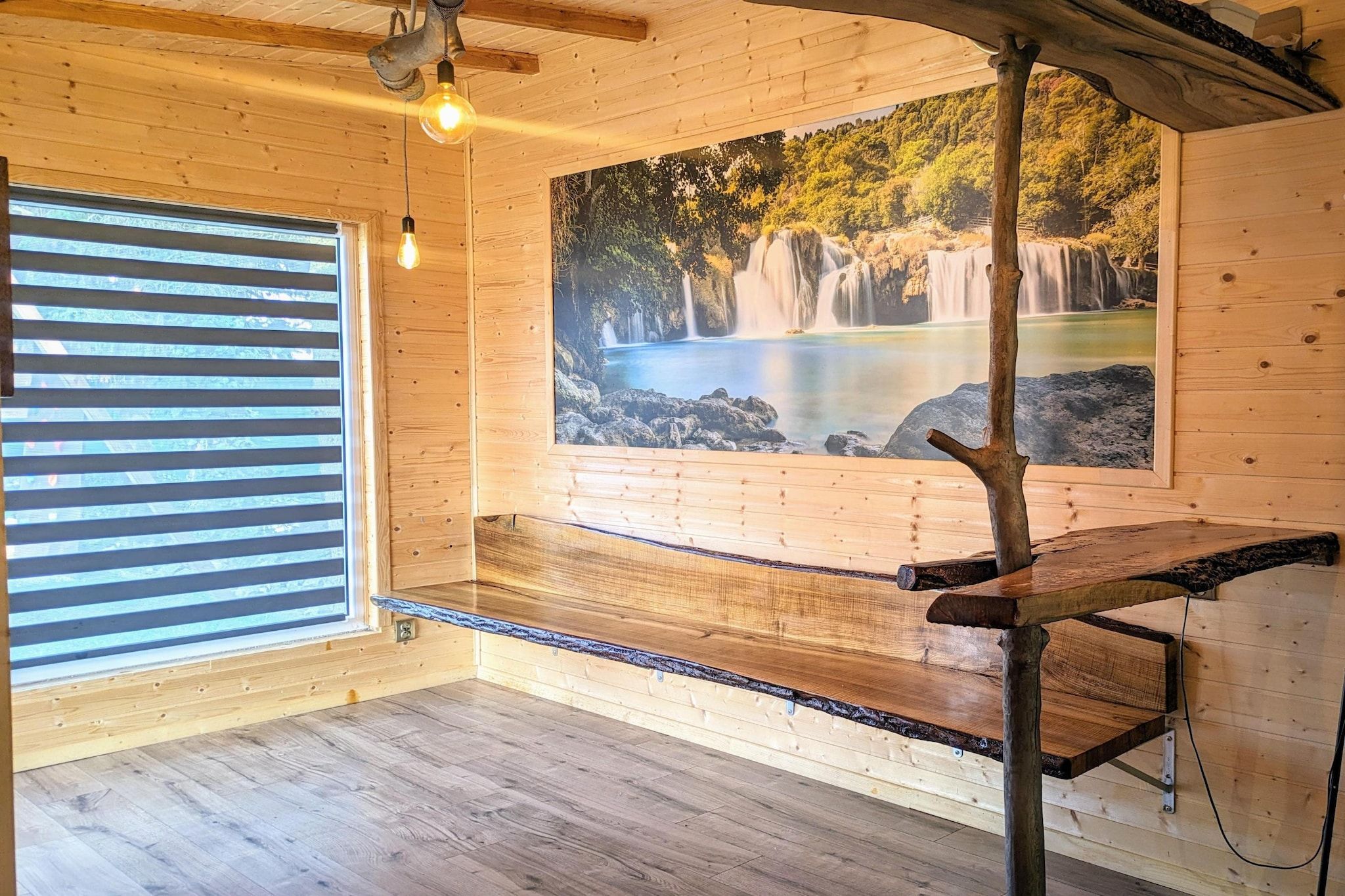 A wooden interior with a bench, a hanging light, and a waterfall mural.
