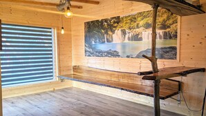 Un interior de madera con un ventanal grande, un banco de madera y una lámpara fijada a la pared.
