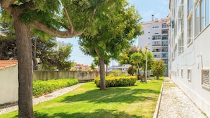 A courtyard with a paved walkway, green grass, and trees. - Great remodeled apartment - 5 min to the beach! (Carcavelos)