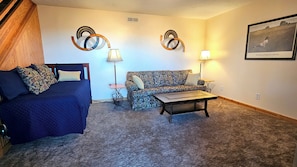 A room with a bed, a sofa, a coffee table, two wall art pieces, and a framed picture on the wall. - Mountain Views, Boone, Blowing Rock & Parkway (Boone)