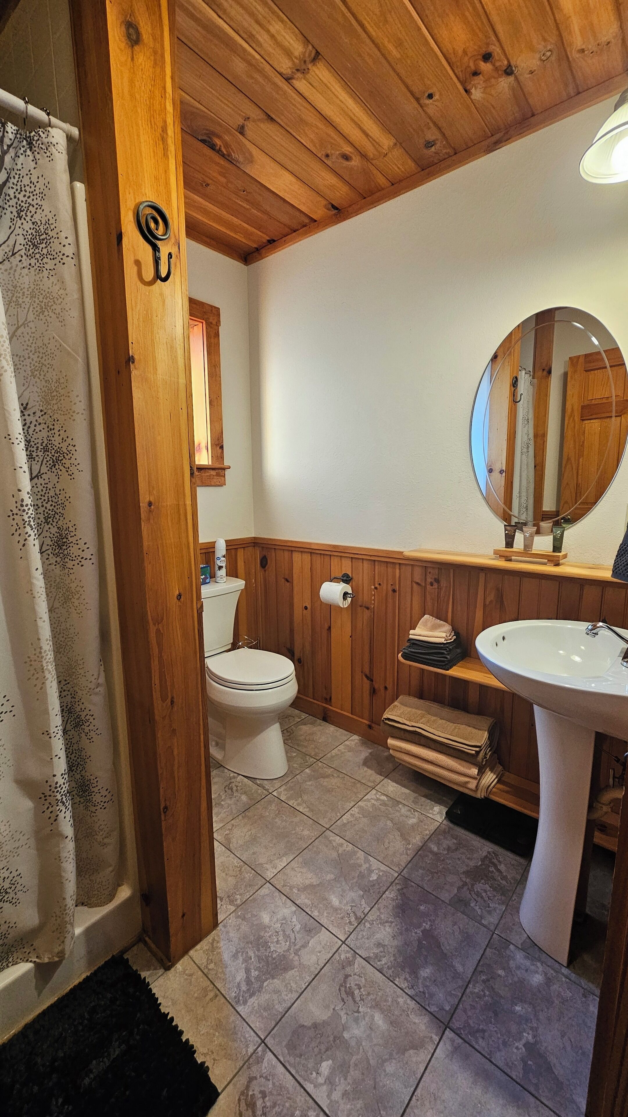 A bathroom with a wooden ceiling, a toilet, a sink, and a mirror.