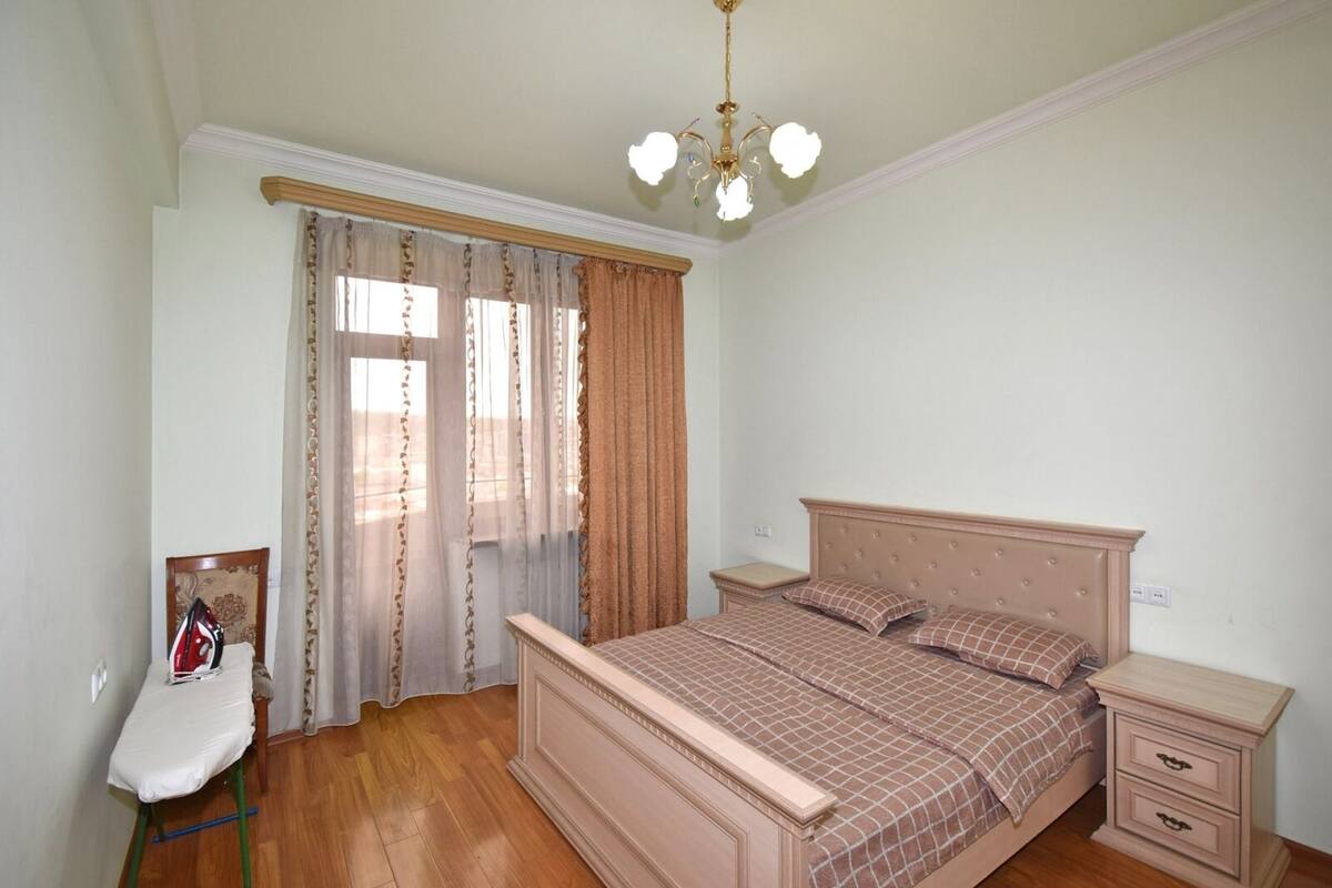 Un dormitorio con cama, mesitas de noche, una silla y una lámpara en el techo.