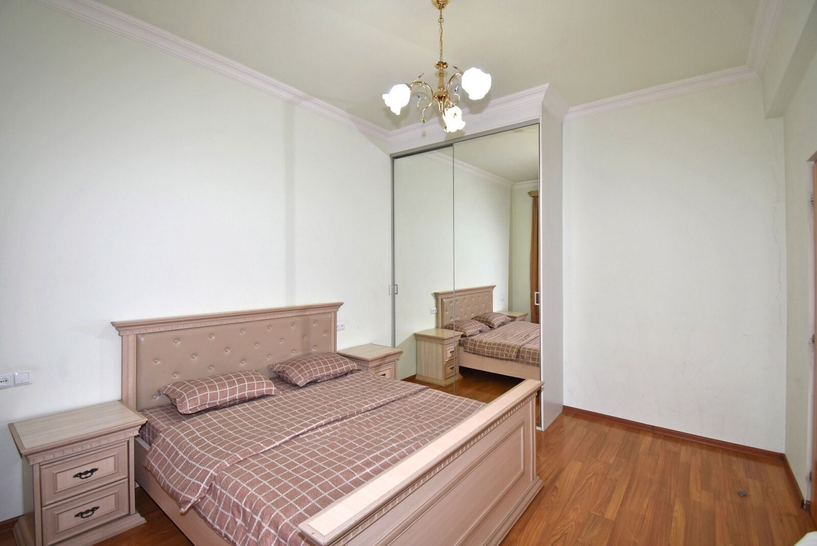 A bedroom with a bed, nightstand, dresser, and a large mirror.