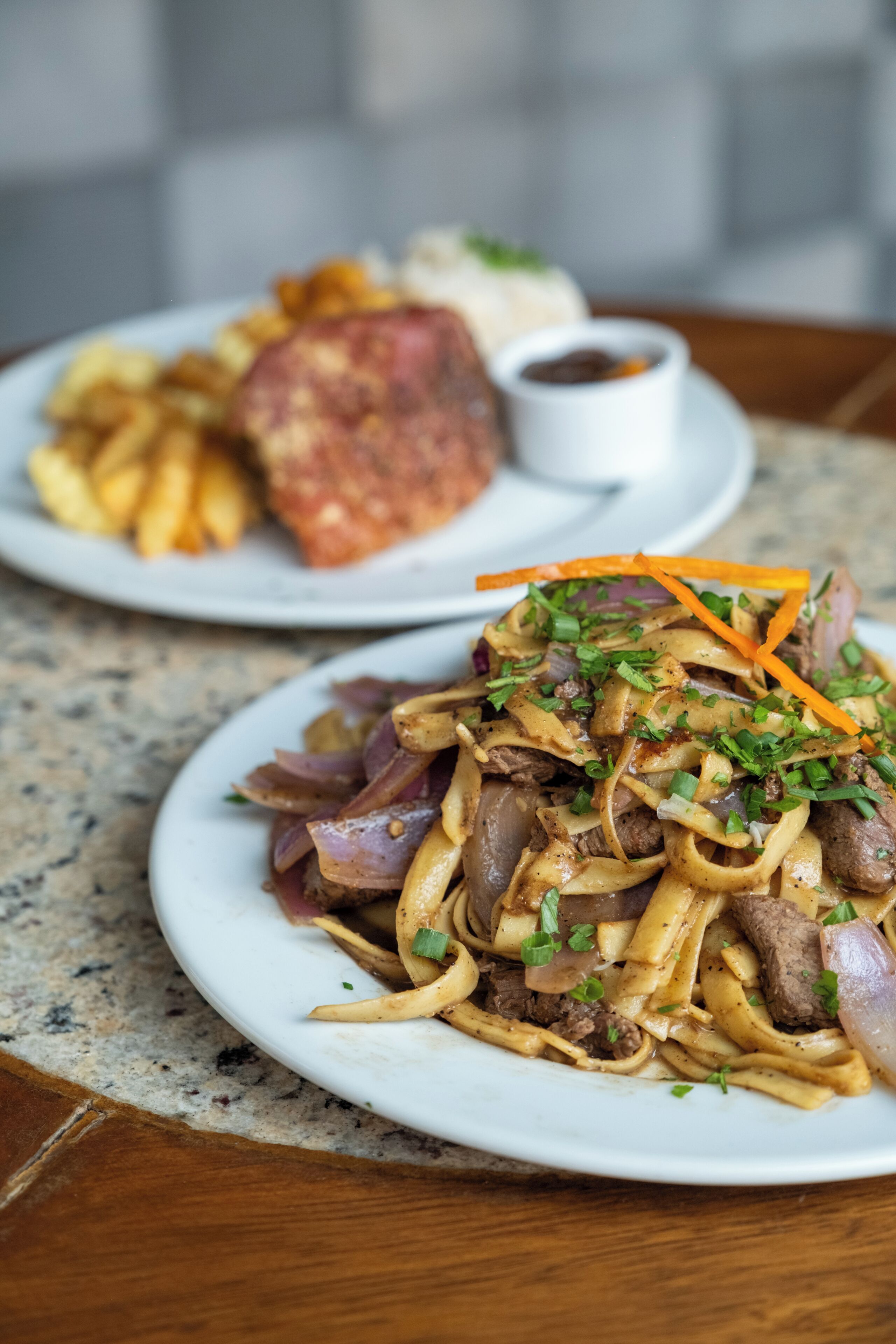 A plate of noodles with beef and vegetables, a side of fries, and a small bowl of sauce.