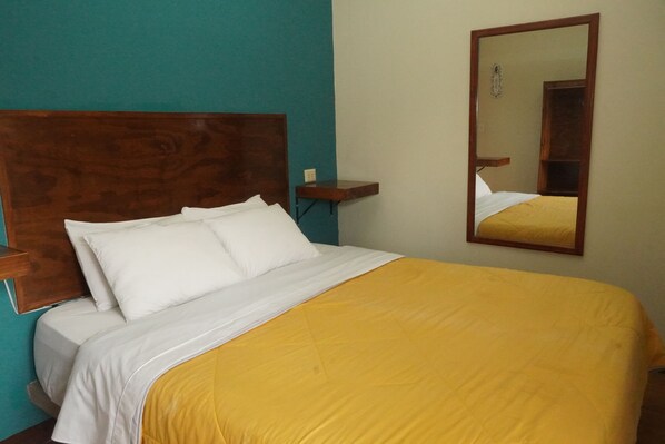 A bed with white and yellow bedding, a wooden headboard, a nightstand, and a mirror on the wall.
