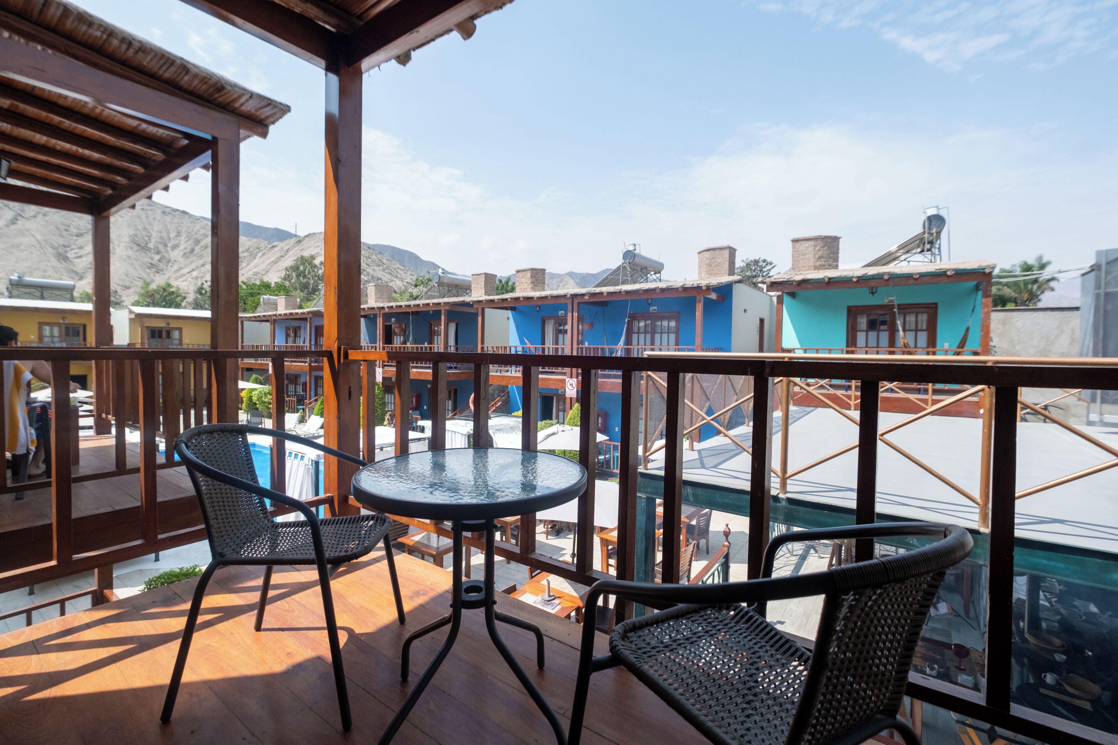 A balcony with two chairs and a table, overlooking a pool and buildings.