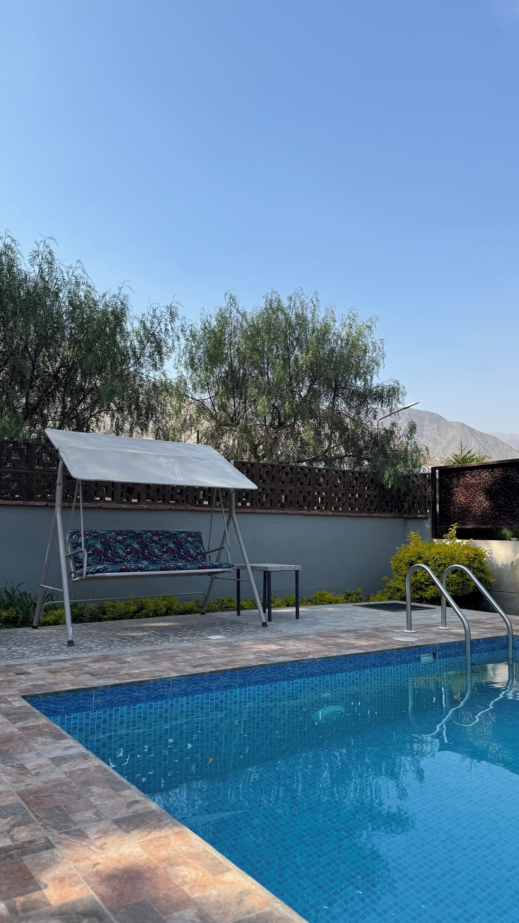 A swimming pool with a sunshade, a lounge chair, and a small table.