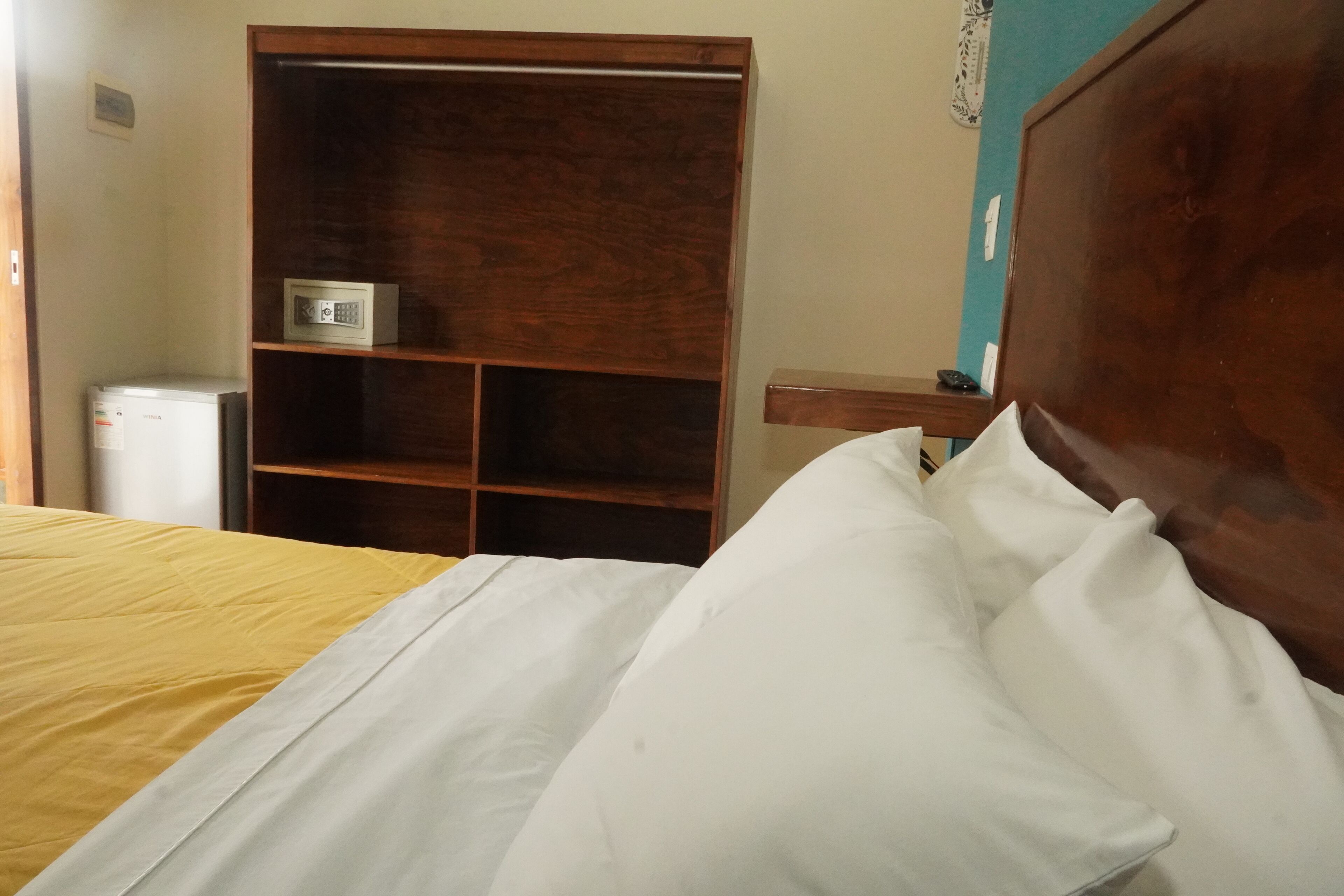Una cama con ropa de cama blanca y amarilla, un cabecero de madera y un armario de madera con un microondas en la repisa superior.