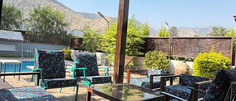 An outdoor patio area with patterned furniture, a glass-top table, and a view of mountains.