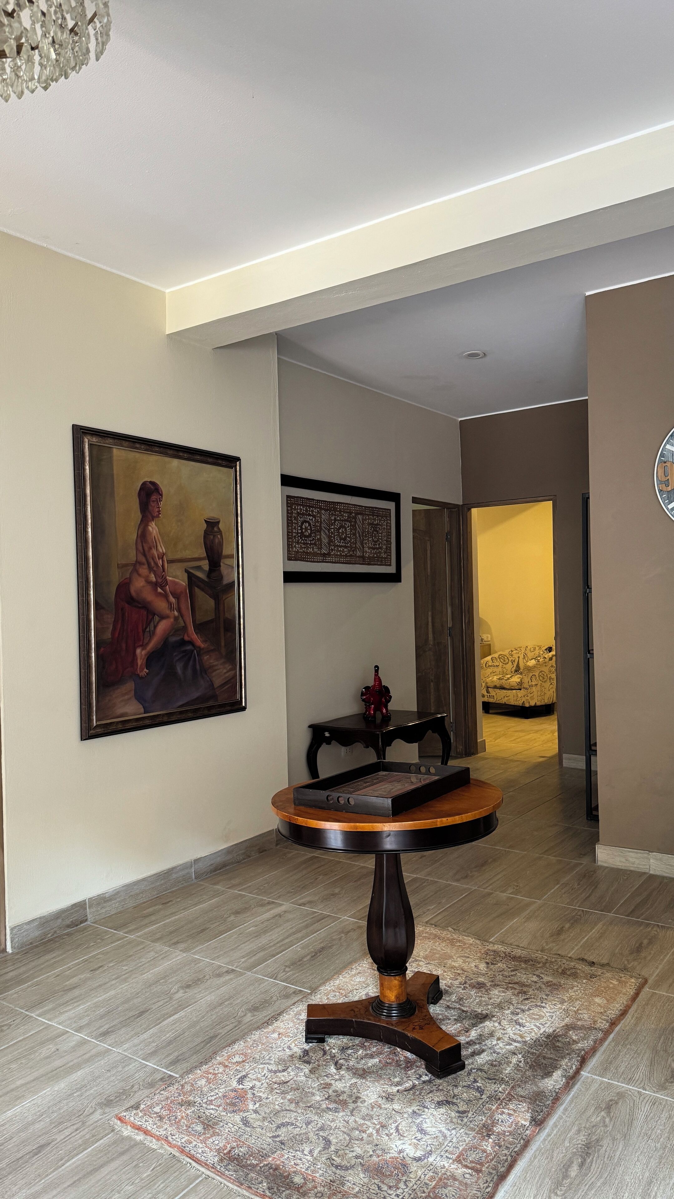 A spacious hallway with a round wooden table, a patterned rug, and artwork on the walls.
