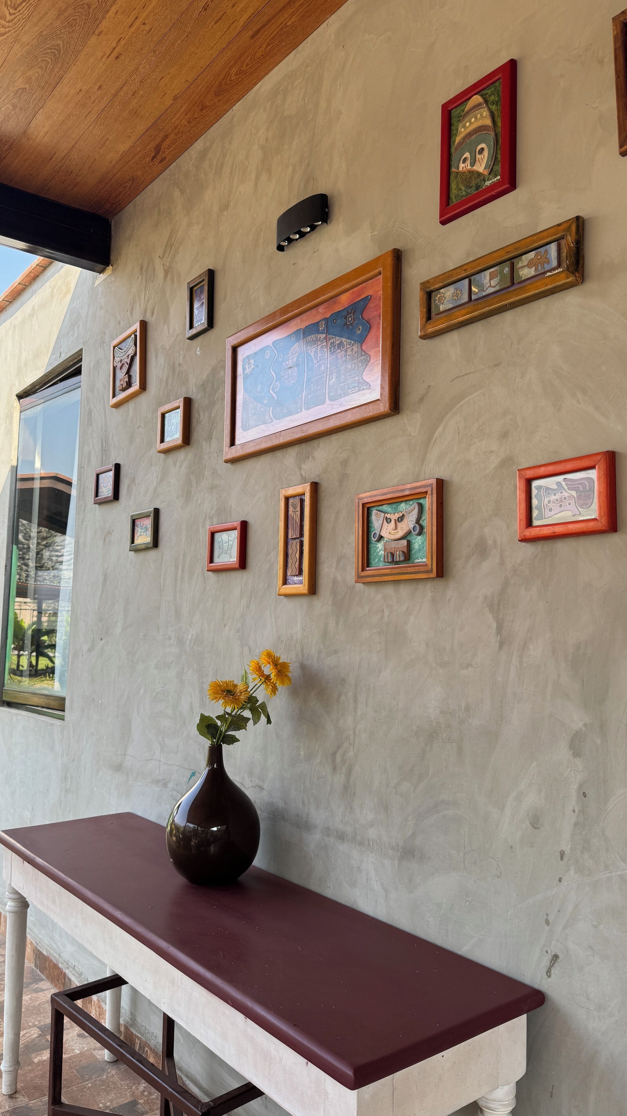 A wall with multiple framed artworks and a vase with flowers on a table.