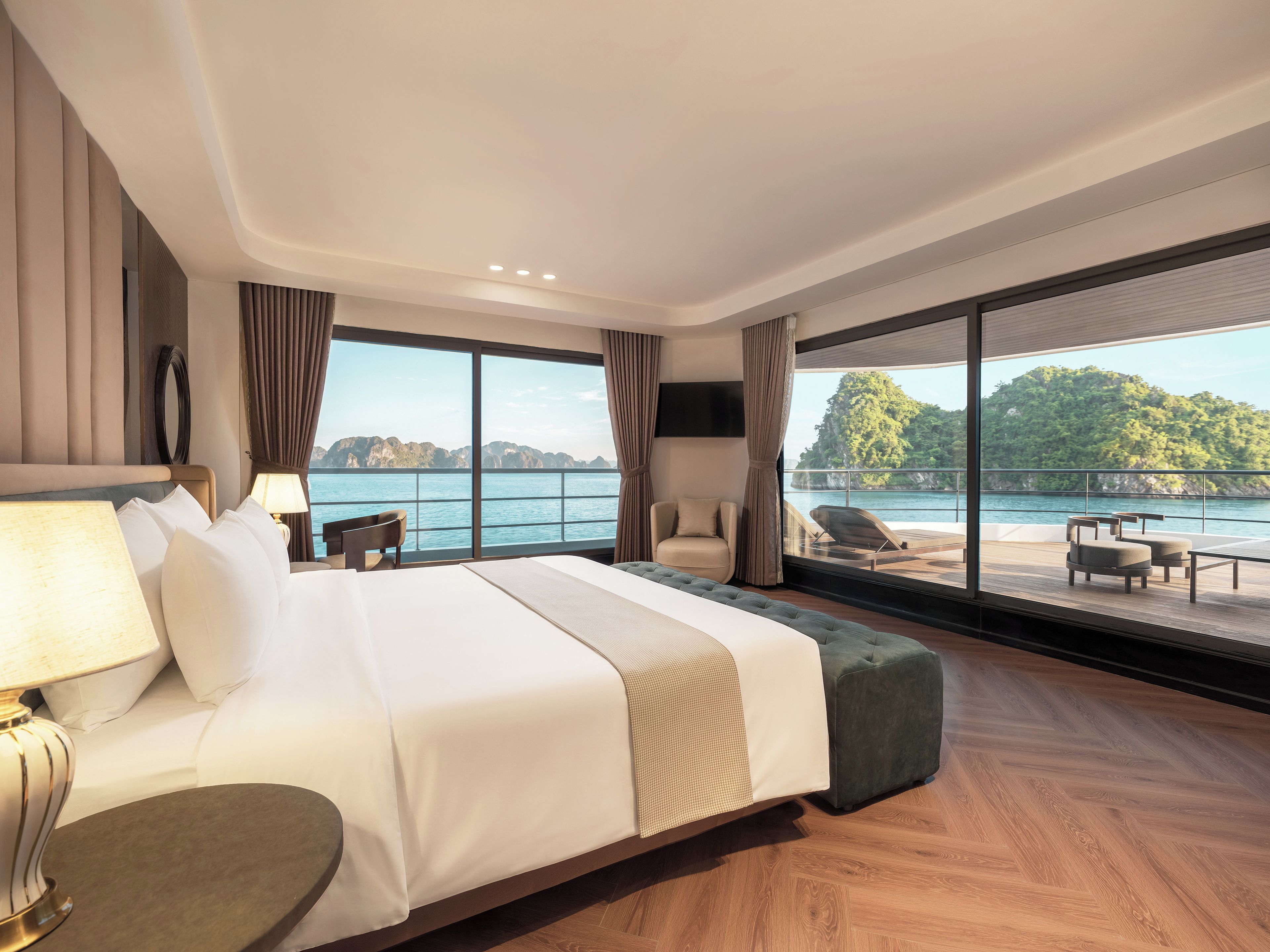A hotel room with a large bed, a sitting area with a view of the sea, and a balcony with outdoor seating.