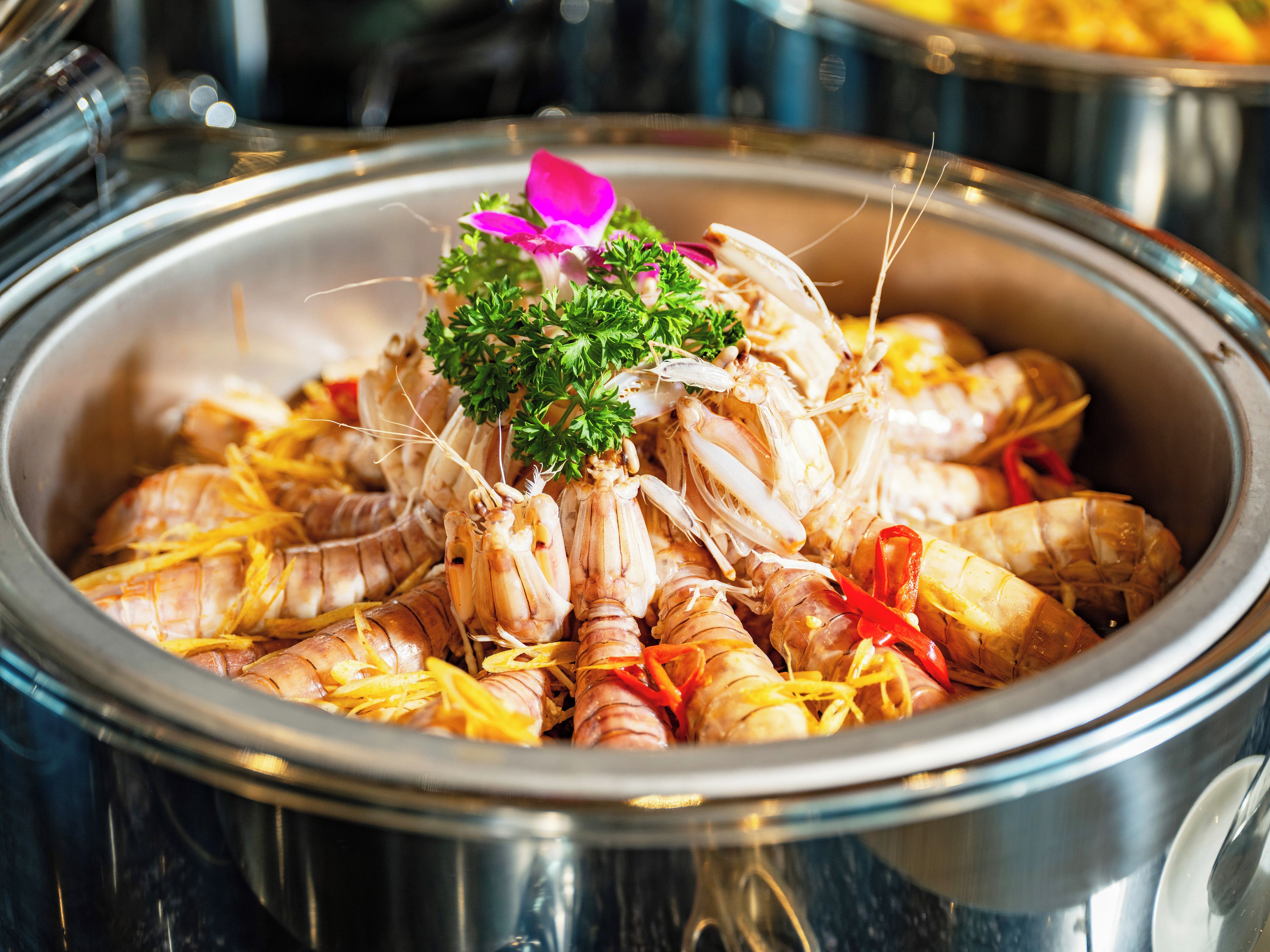 A large metal pot filled with cooked shrimp garnished with parsley and lemon slices.