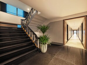 L’intérieur moderne d’un hôtel, avec un escalier, une plante en pot et un couloir menant à une porte.