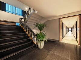 A modern hotel interior with a staircase, a potted plant, and a hallway leading to a door.