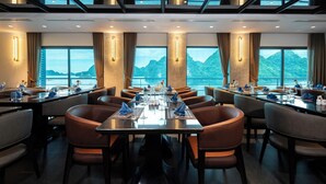 A dining area with tables set for multiple guests, large windows with a mountain view, and modern ceiling design. - Celina of The Sea Cruise (Tuan Chau)