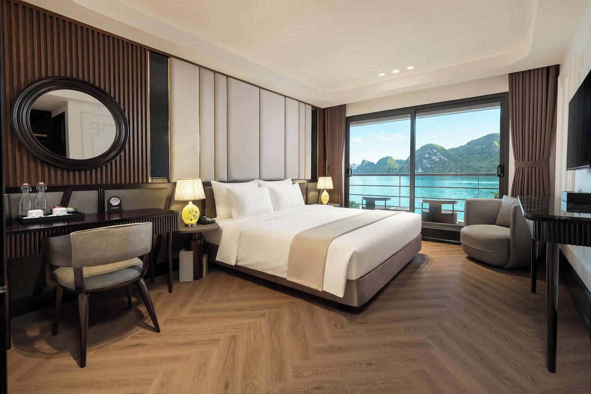 Une chambre d’hôtel avec un grand lit, un bureau avec une chaise, une télévision et une vue sur la mer.