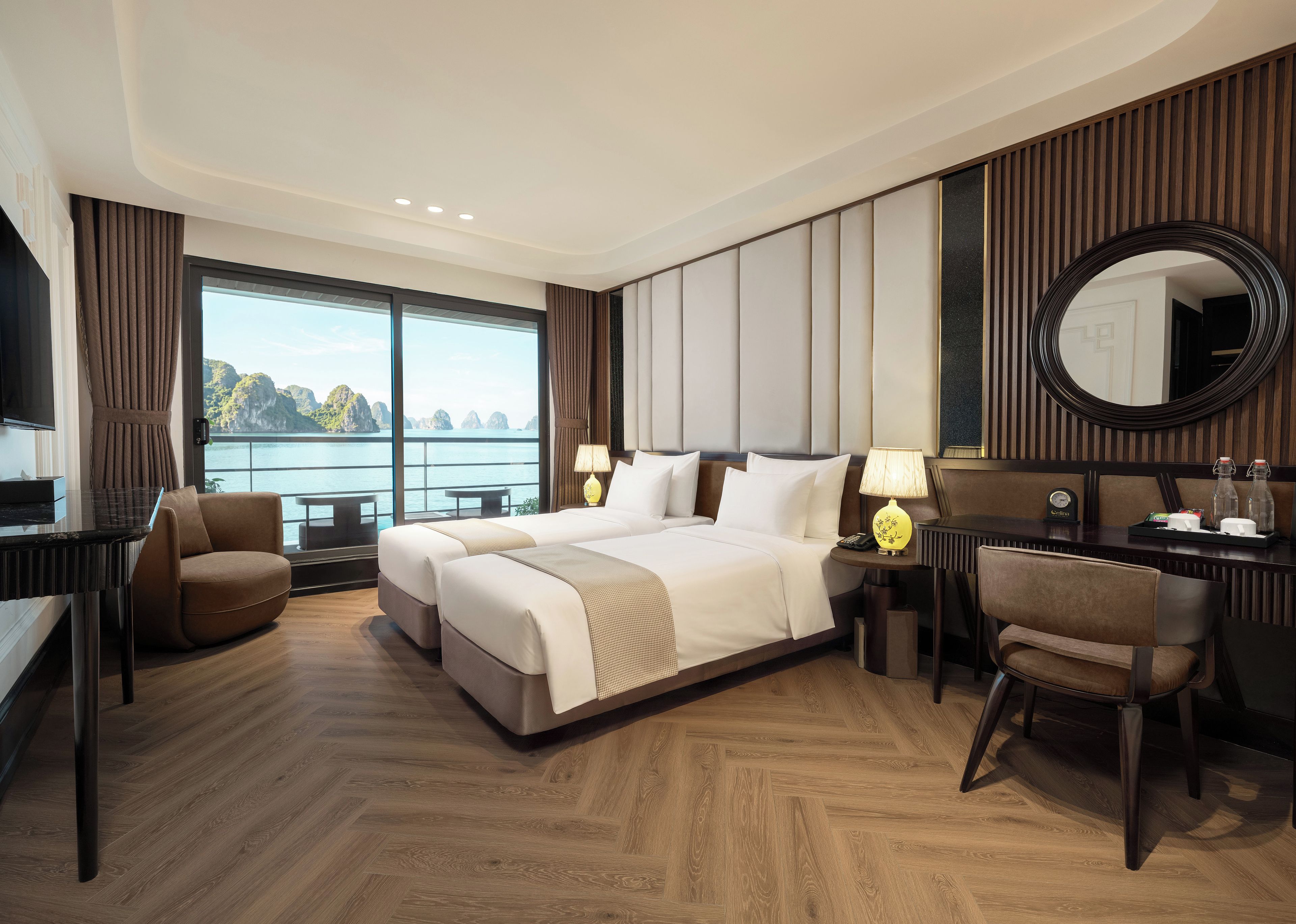 Habitación de hotel con una cama, dos mesitas de noche, un escritorio, una silla, un televisor y un ventanal con vistas al mar.