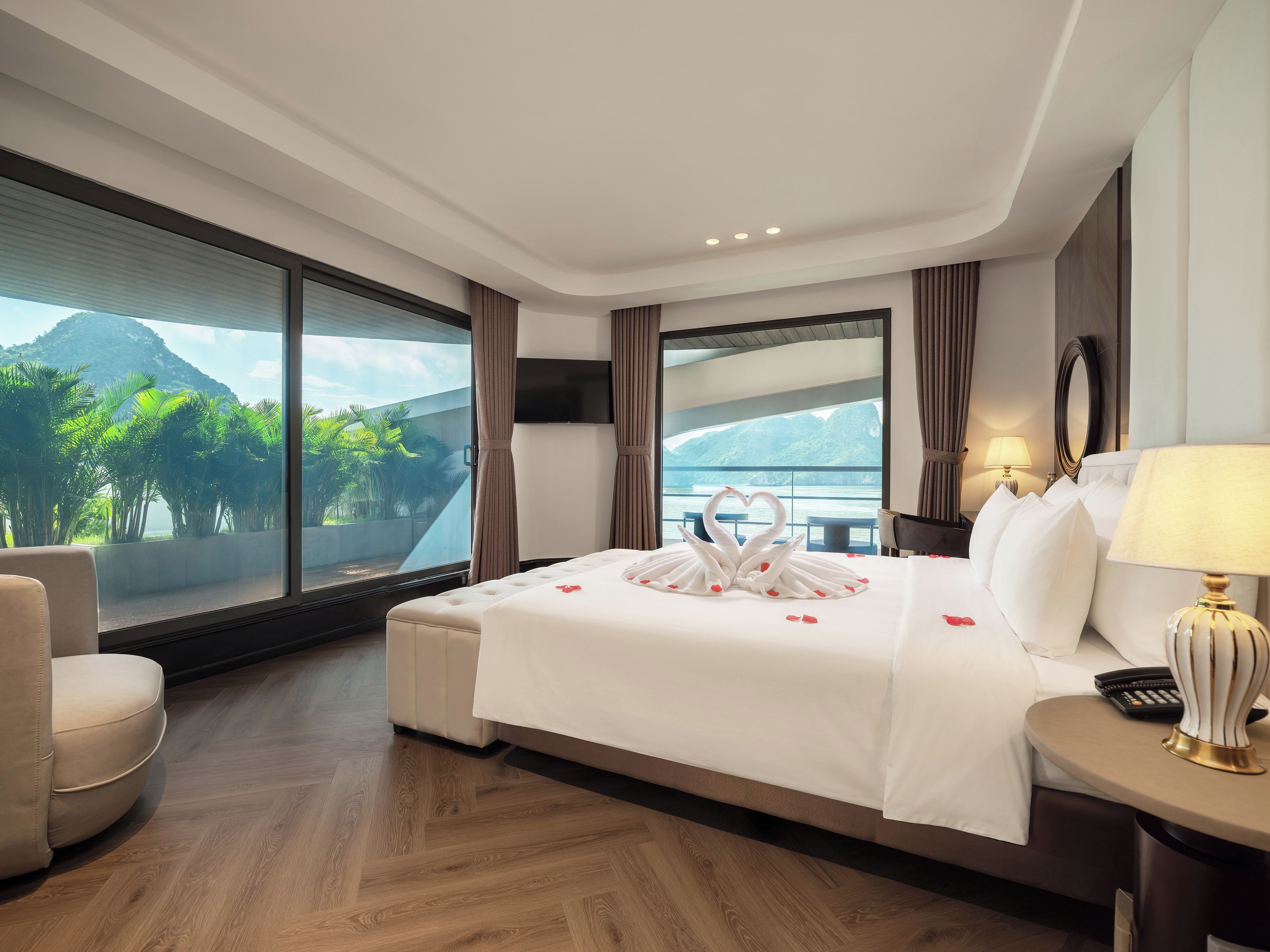 A hotel room with a large bed, a sitting area, a view of the sea, and a balcony.
