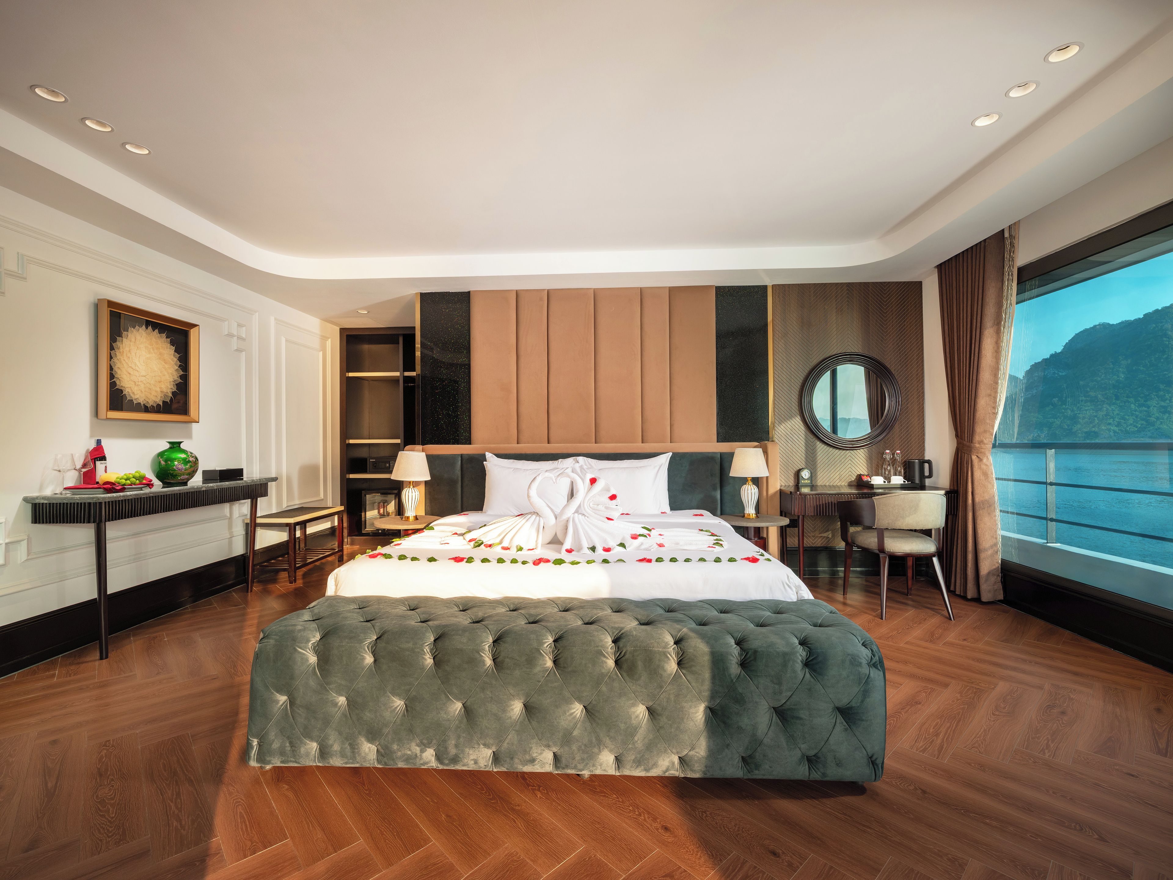 Une chambre d’hôtel moderne avec un grand lit, un bureau, une chaise, un miroir rond et une vue sur l’eau.
