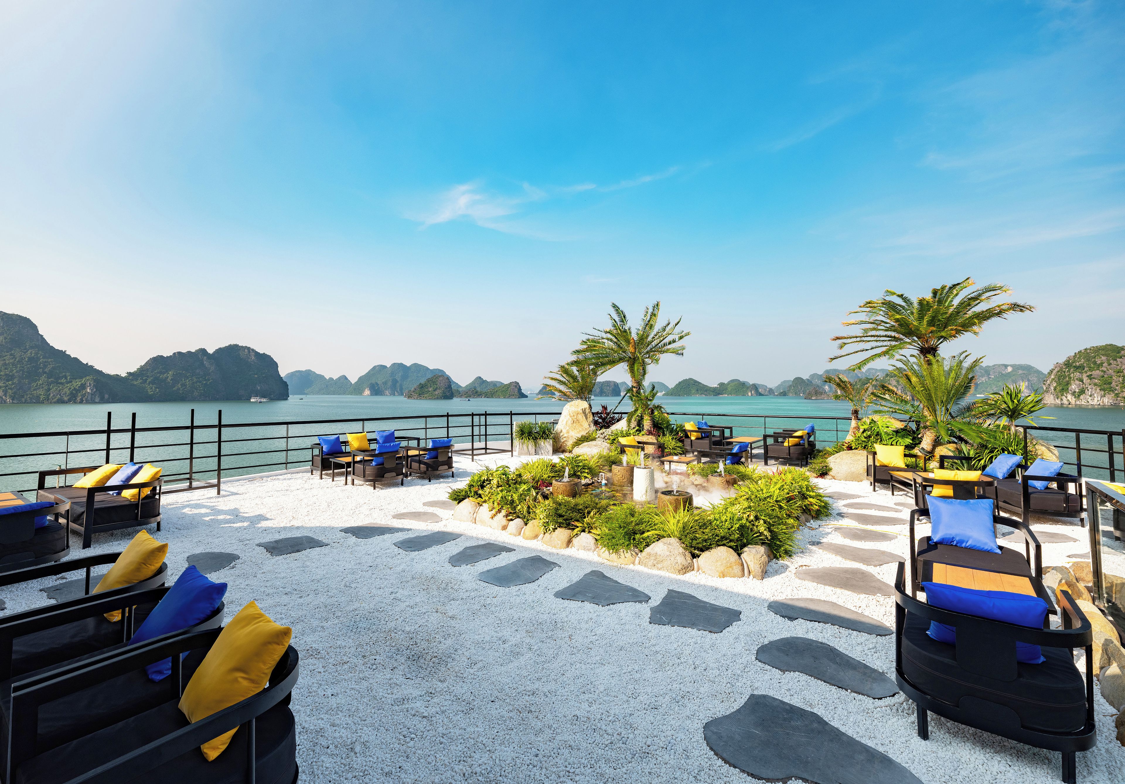 A terrace with outdoor seating, a view of the sea, and a mountainous landscape in the background.