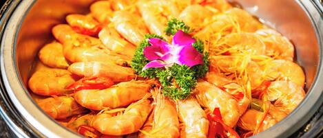 A large, round, metallic container filled with cooked shrimp, garnished with parsley and a purple flower.