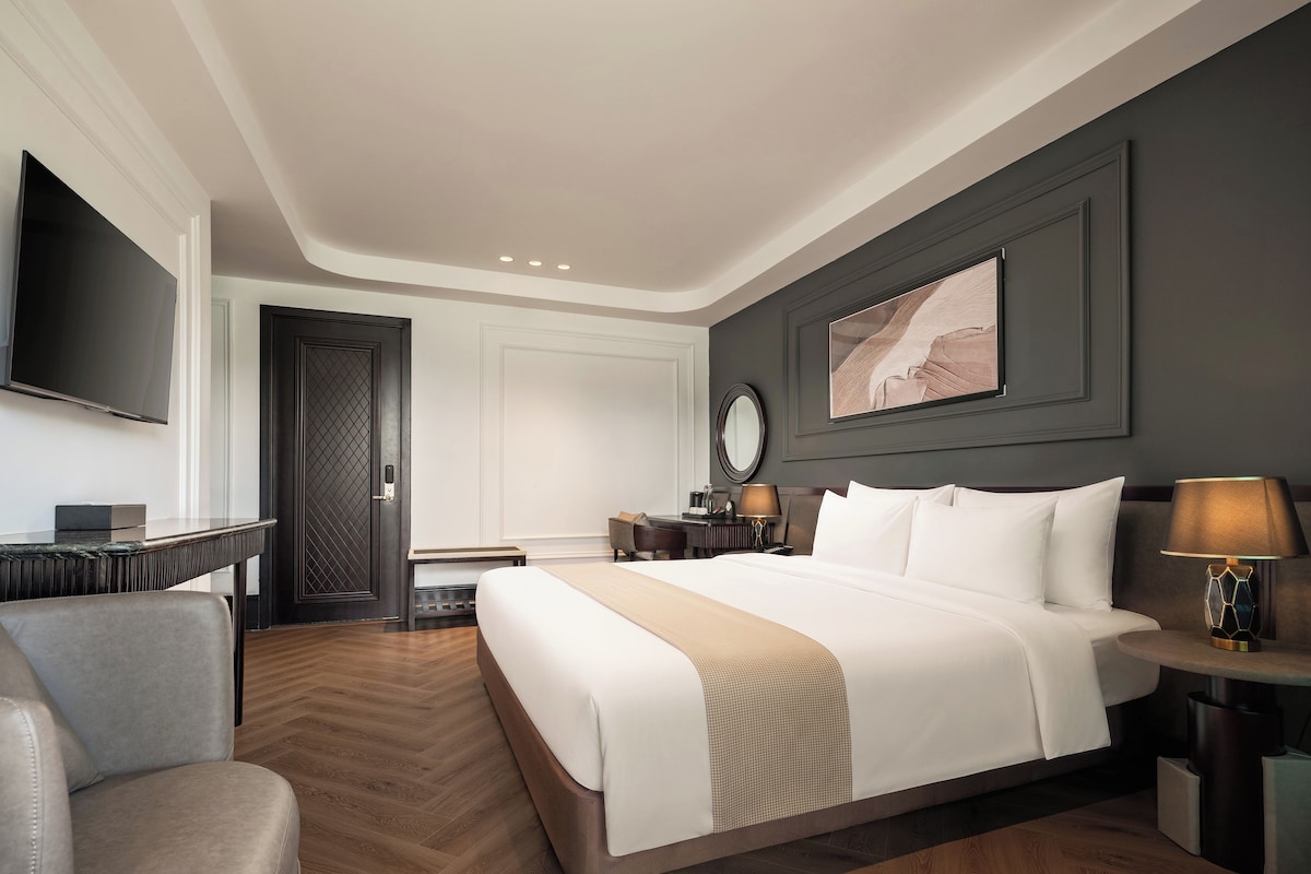 Une chambre d’hôtel avec un grand lit, un bureau, une chaise, une télévision et un tableau au mur.