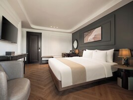 Habitación de hotel con una cama grande, un escritorio, una silla, un televisor, una lámpara de escritorio y un cuadro en la pared.
