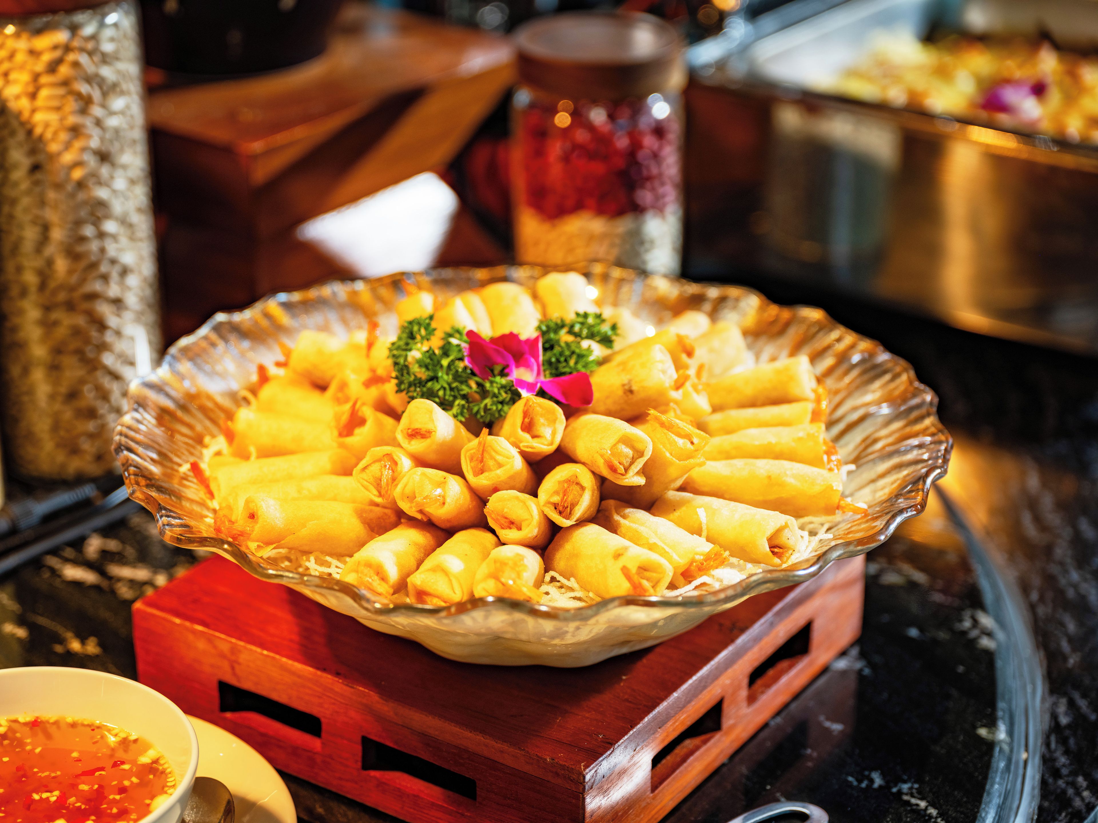 A glass bowl filled with spring rolls on a wooden table.