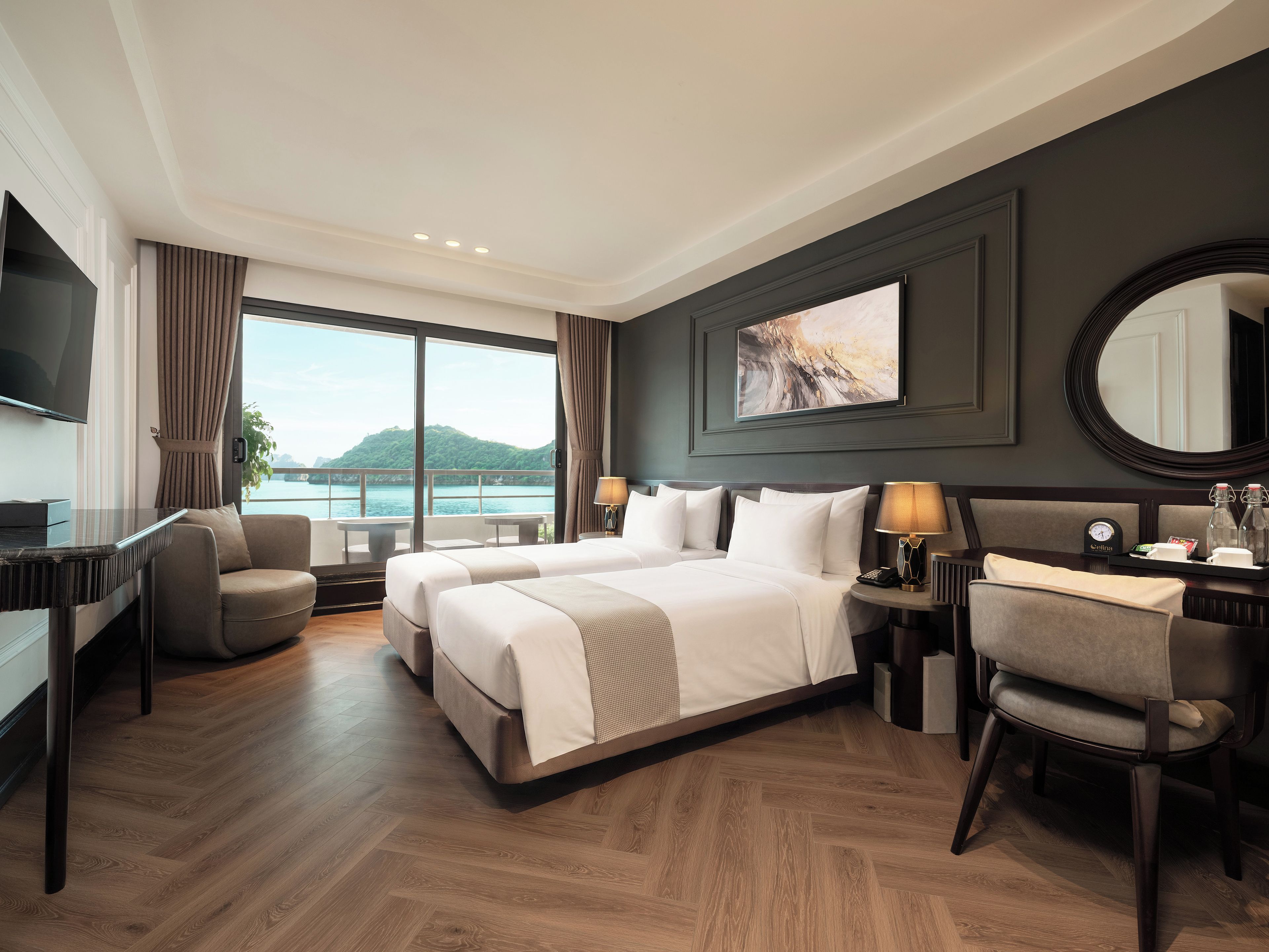 A hotel room with a large bed, a desk, a chair, a TV, and a view of a body of water.