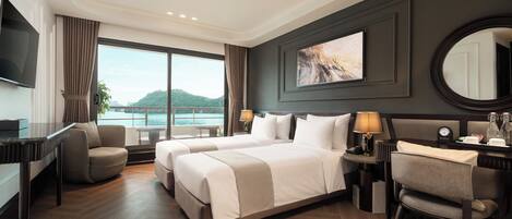 A hotel room with a large bed, a desk, a chair, a TV, and a view of a body of water.