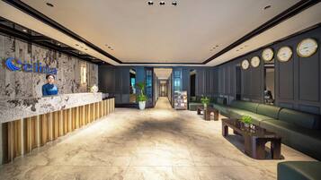 Zona de recepción de un hotel con piso de mármol, mostrador de recepción, un sofá verde y relojes de pared.