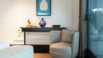 A room with a sofa, a chair, a console table with decorative items, a framed artwork, and a window with a view.