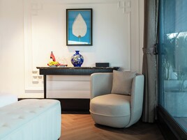 A room with a sofa, a chair, a console table with decorative items, a framed artwork, and a window with a view.