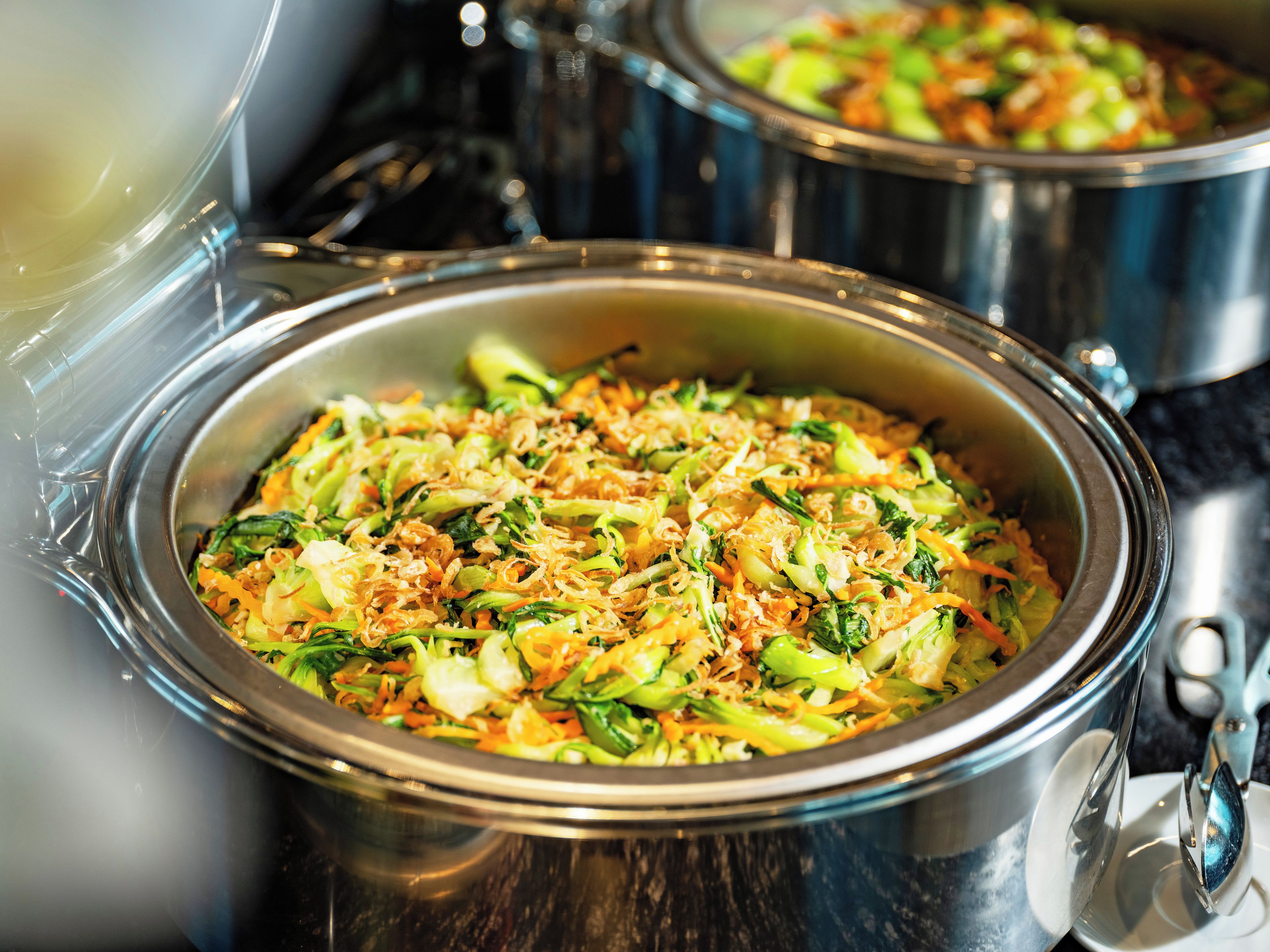 A buffet with various dishes, including a vegetable stir-fry and a dish with noodles.