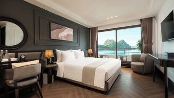 A hotel room with a large bed, a desk, a chair, a TV, and a view of the sea.