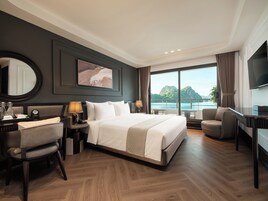Habitación de hotel con una cama grande, un escritorio, una silla, un televisor y vista al mar.
